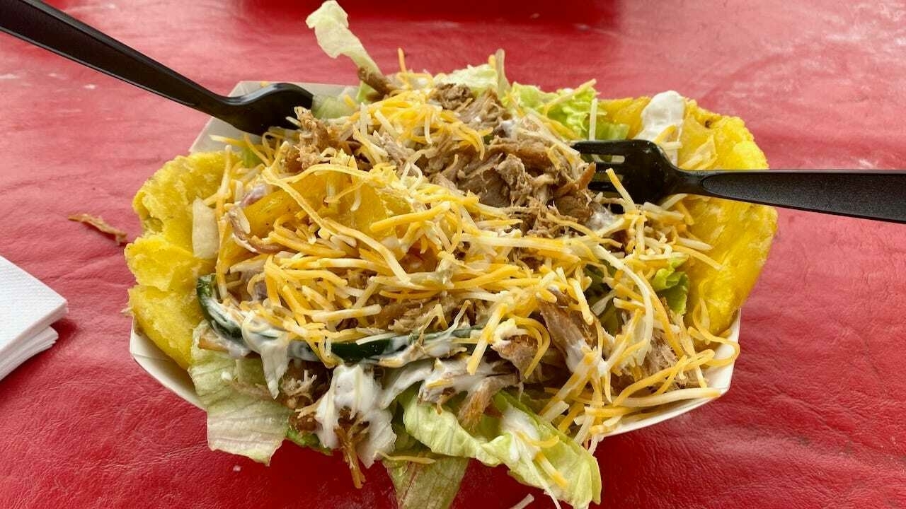 A yellow tortilla bowl filled with shredded meat, lettuce, and a creamy sauce, topped with cheddar cheese.