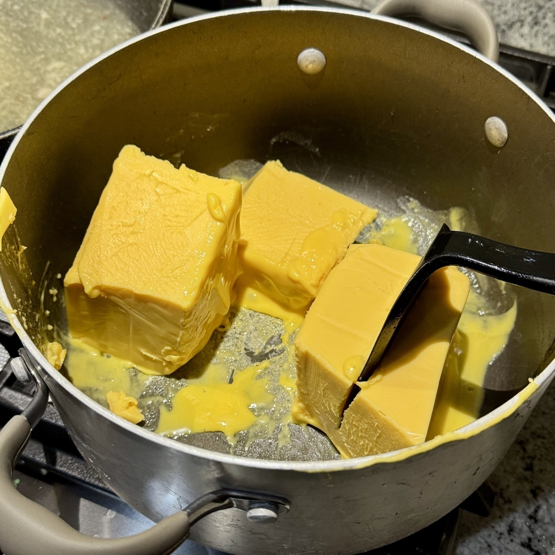 Three blocks of yellow cheese float in a pan of melted butter on a stovetop.