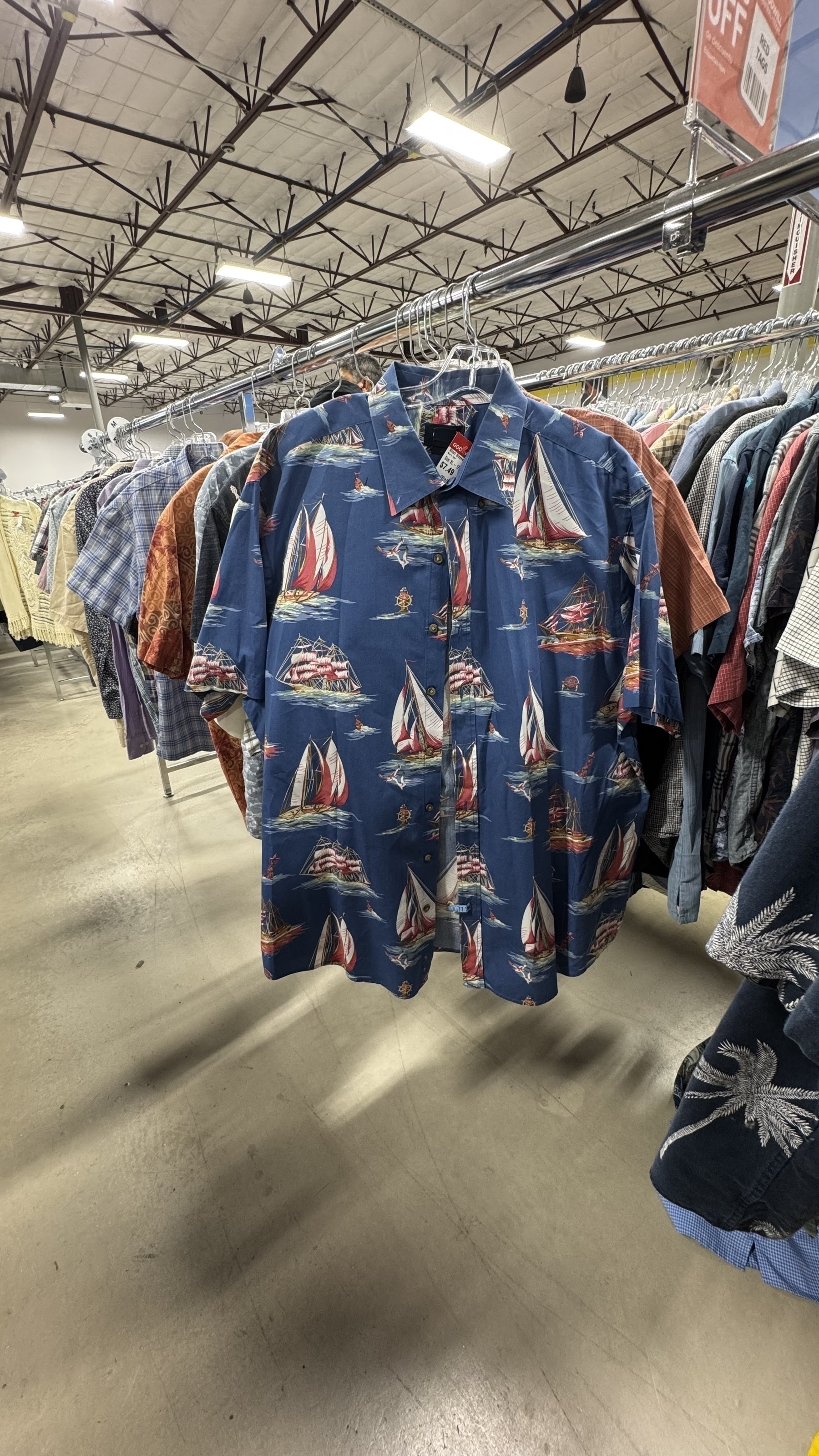 A blue Hawaiian shirt with sailboats hangs on a clothing rack, with a "sale" tag visible.