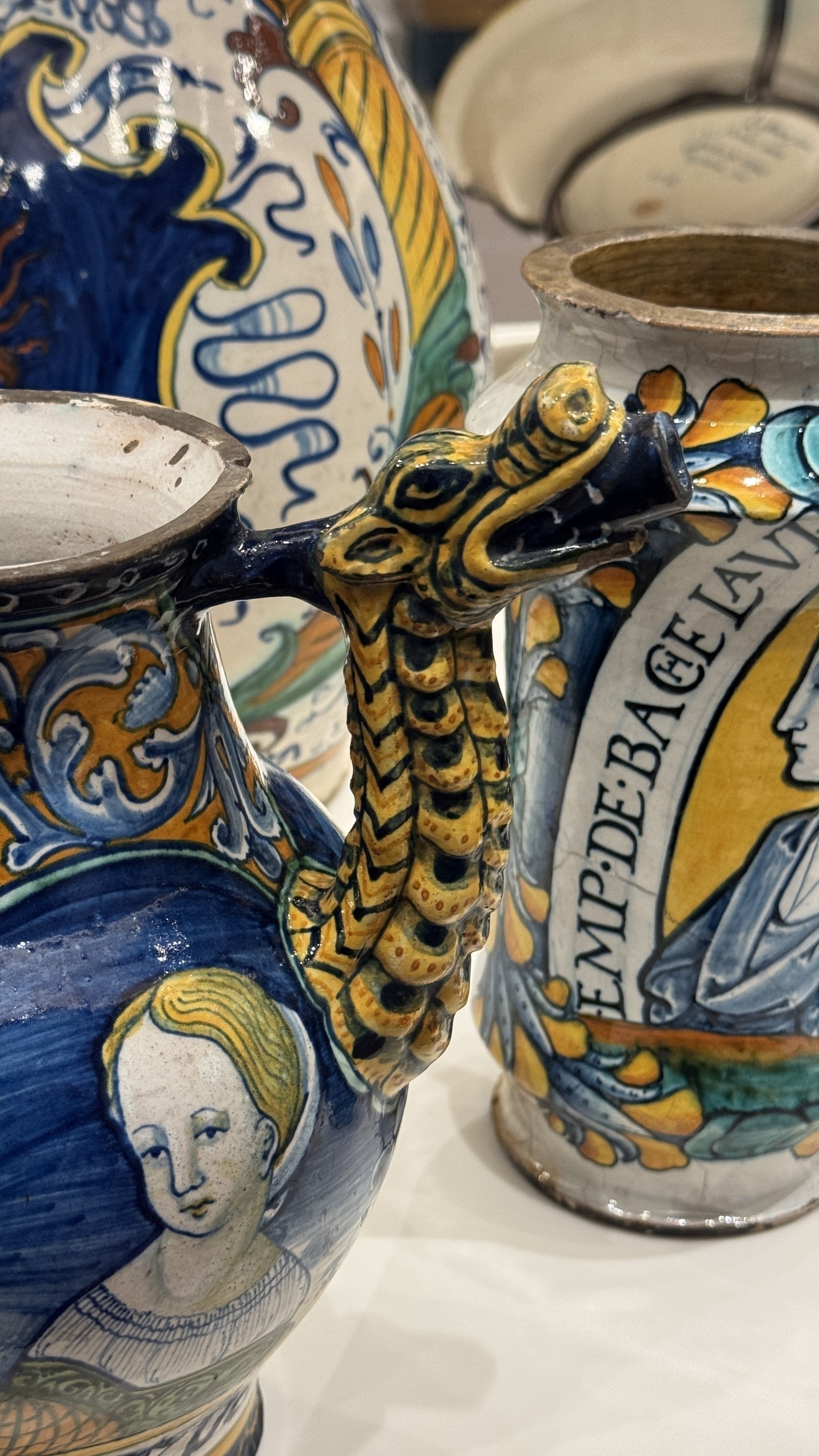 Two painted ceramic jugs feature a serpent handle and a portrait of a woman with the word “EMPRE” visible.