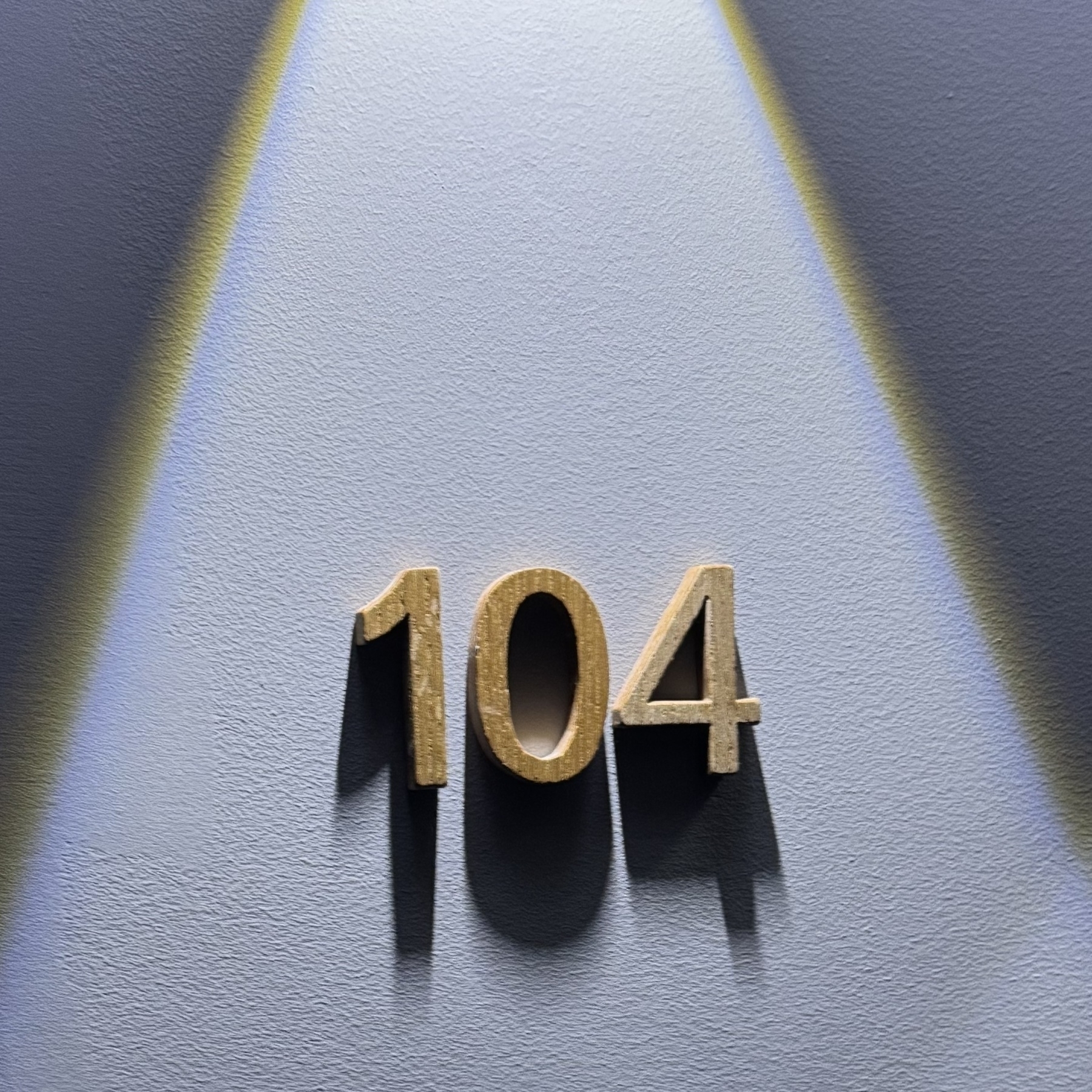 Gold-colored number 104 is illuminated against a blue wall with yellow light streaks.