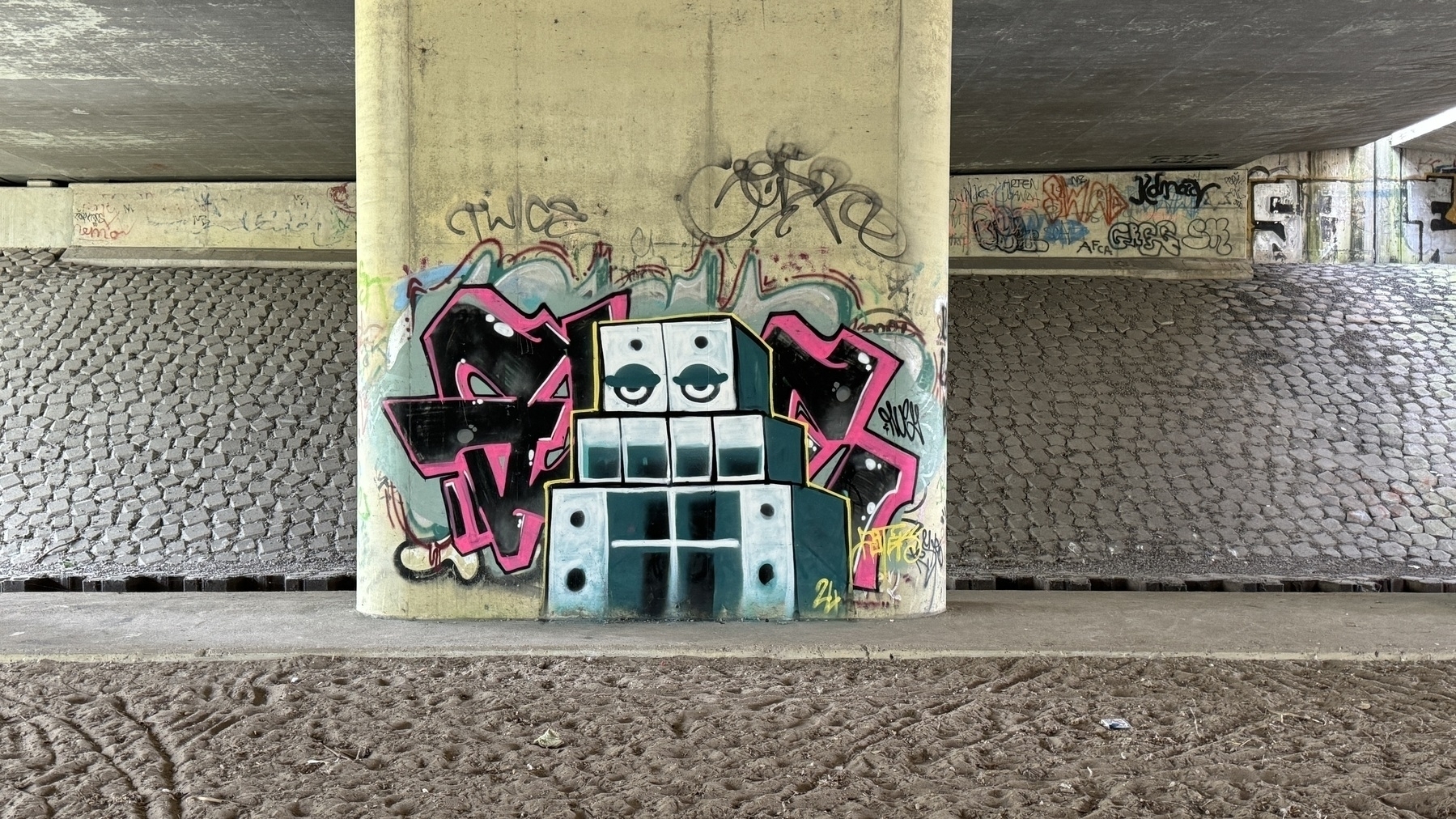 A concrete pillar is covered in graffiti, including a stylized building with multiple windows and the word "Sly.