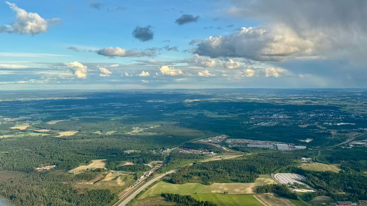 Aerial view of a forested landscape with a town and industrial area below, under cloudy skies.