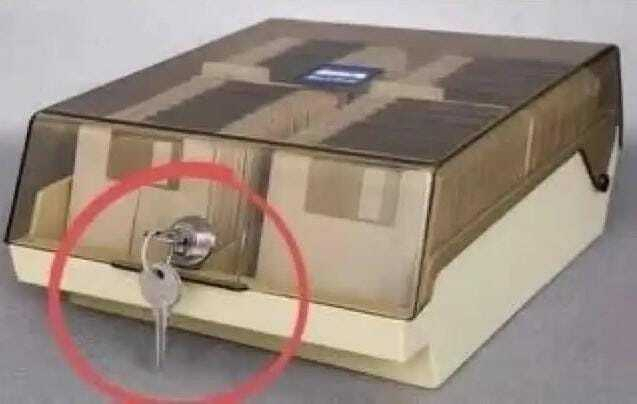 A beige, plastic safe with a key and a small blue label is displayed on a white surface.
