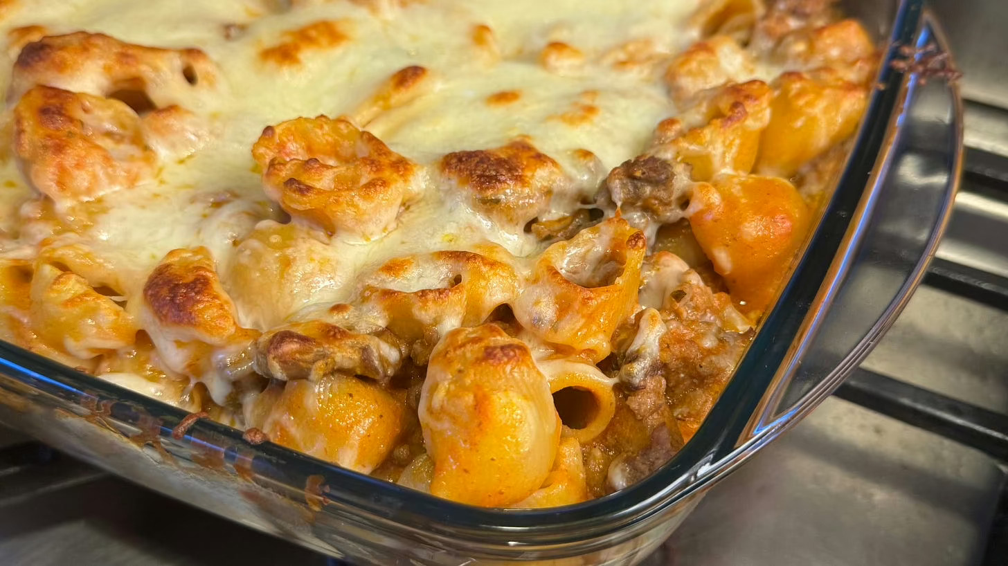 A glass baking dish contains baked pasta with tomato sauce and cheese.