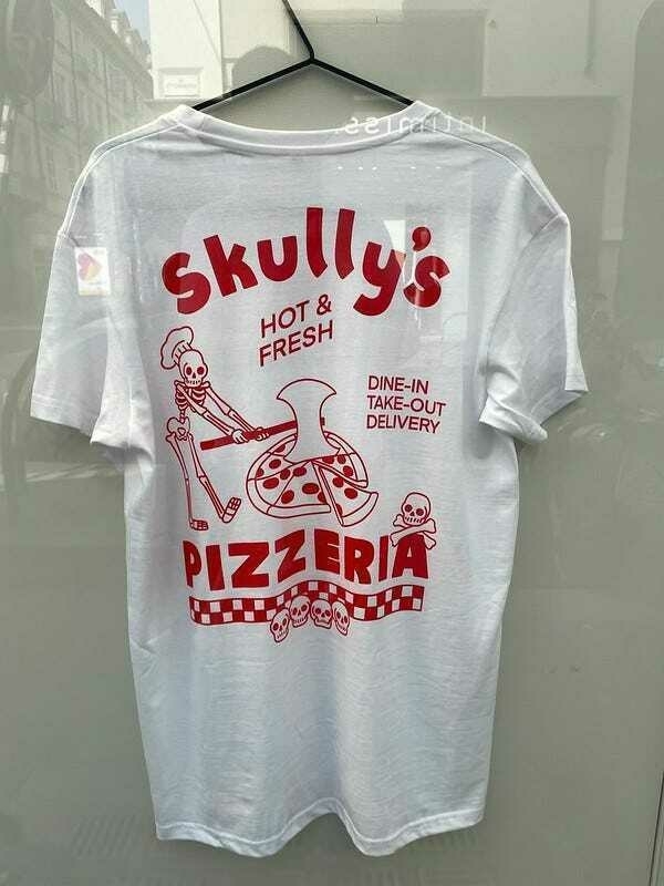 A white t-shirt displays “Skully’s Hot & Fresh” with a cartoon skeleton holding a pizza slice and the words “DINE-IN TAKE-OUT DELIVERY”.
