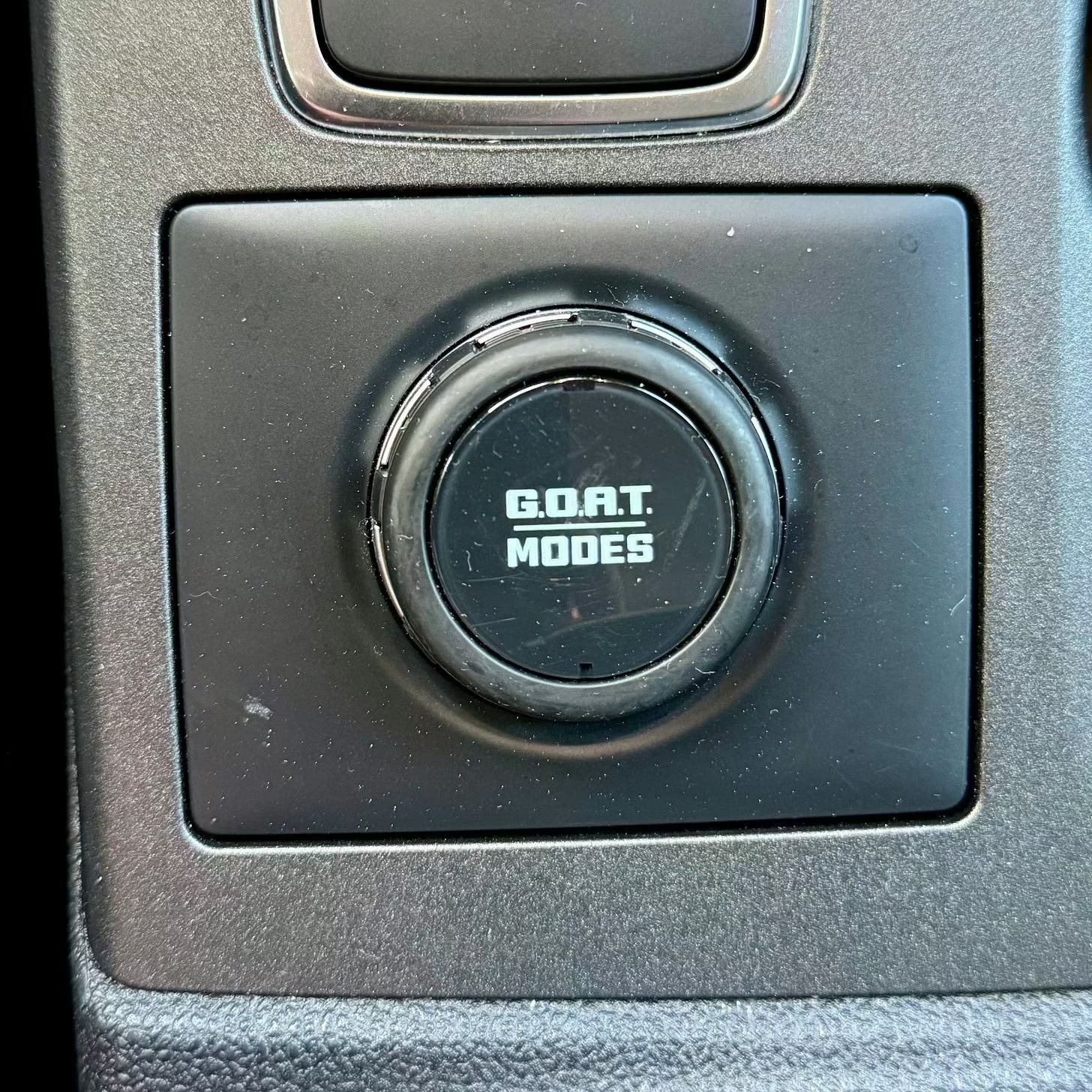 A black button with the text “G.O.A.T. MODES” is visible on a dark gray interior surface.
