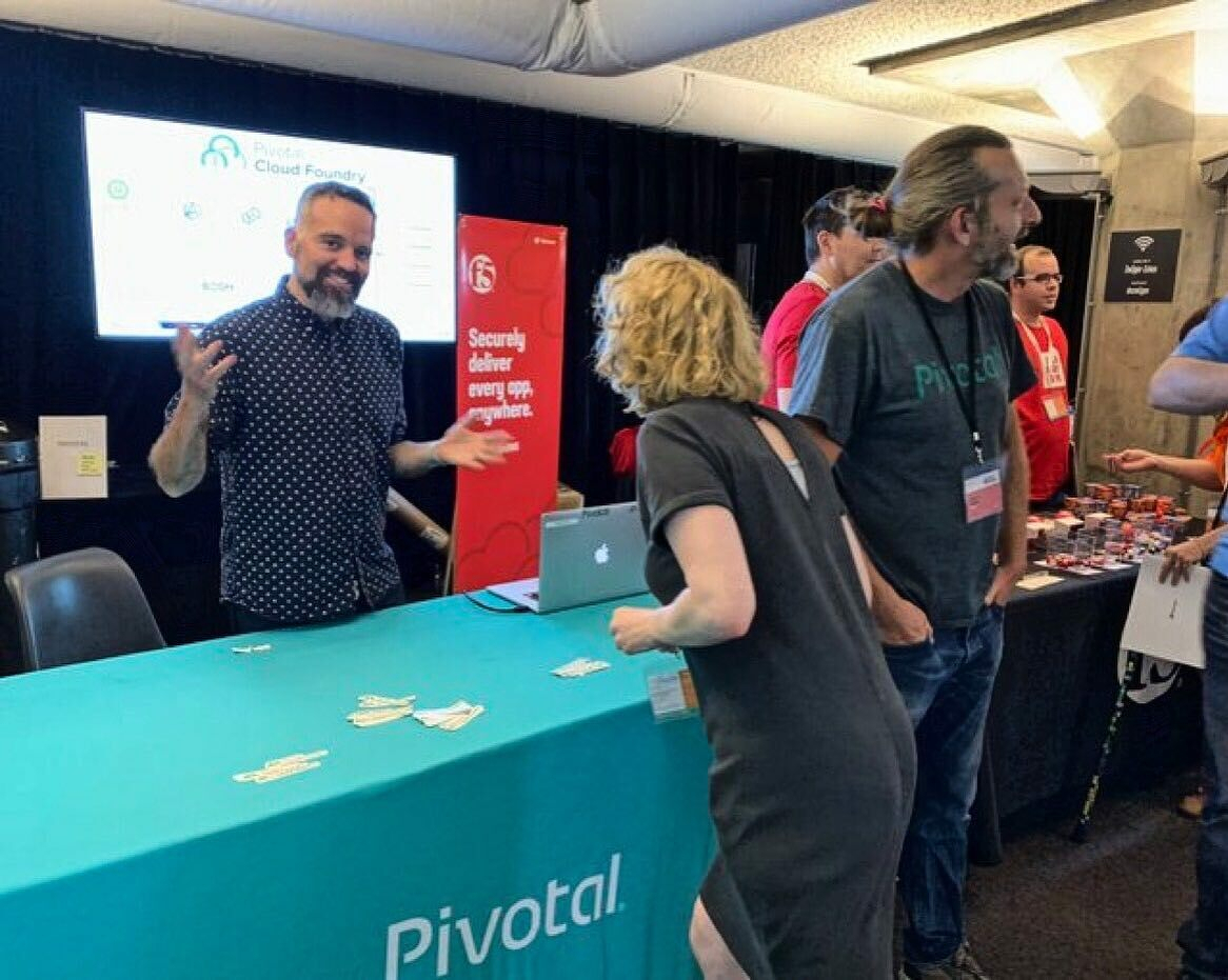 A man gestures at a Pivototal booth with a blue table displaying the company logo and the text "Securely deliver every app.