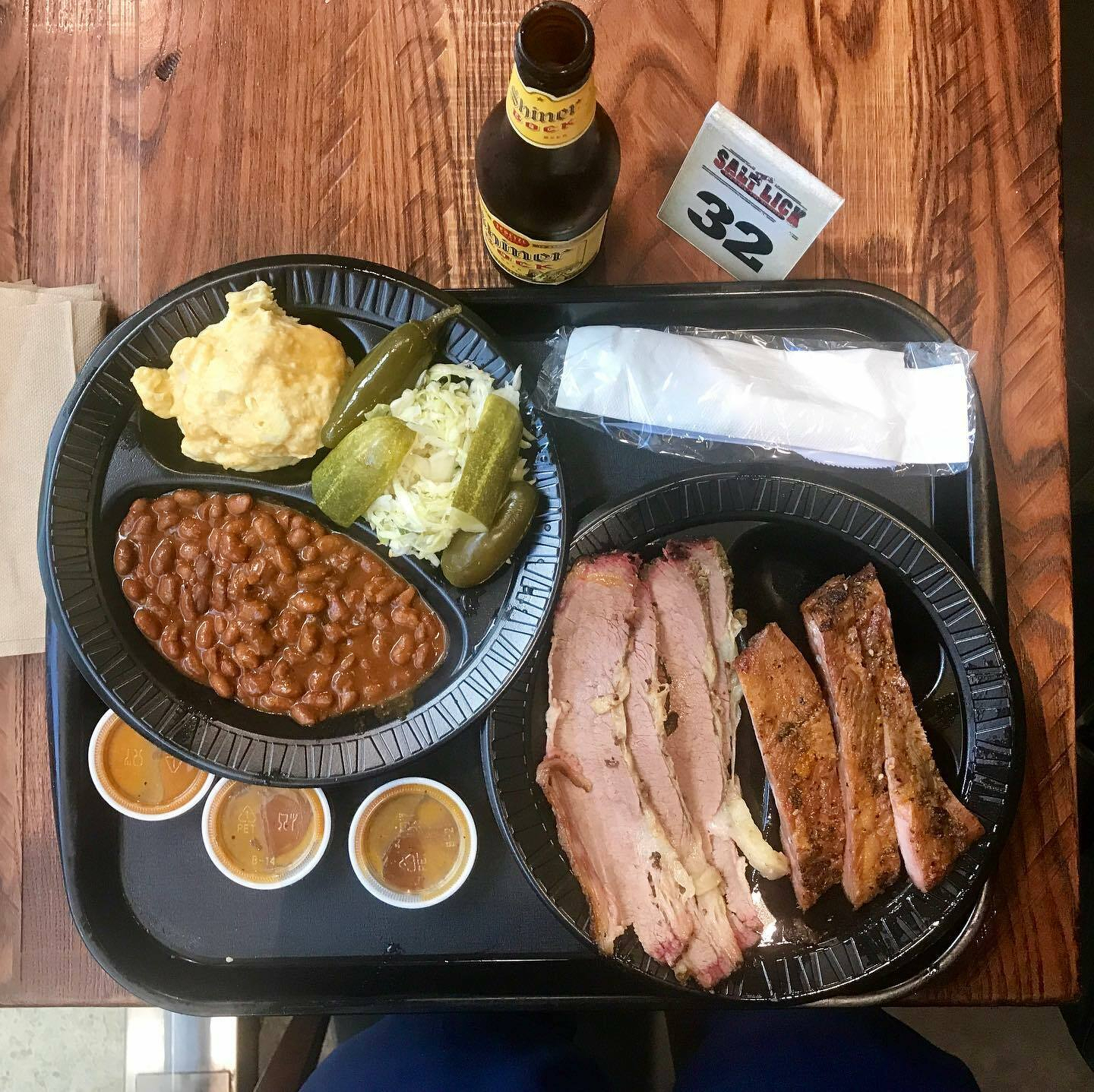 Smoked brisket with beans, slaw, and a Salt Lick BBQ container sits on a black tray.