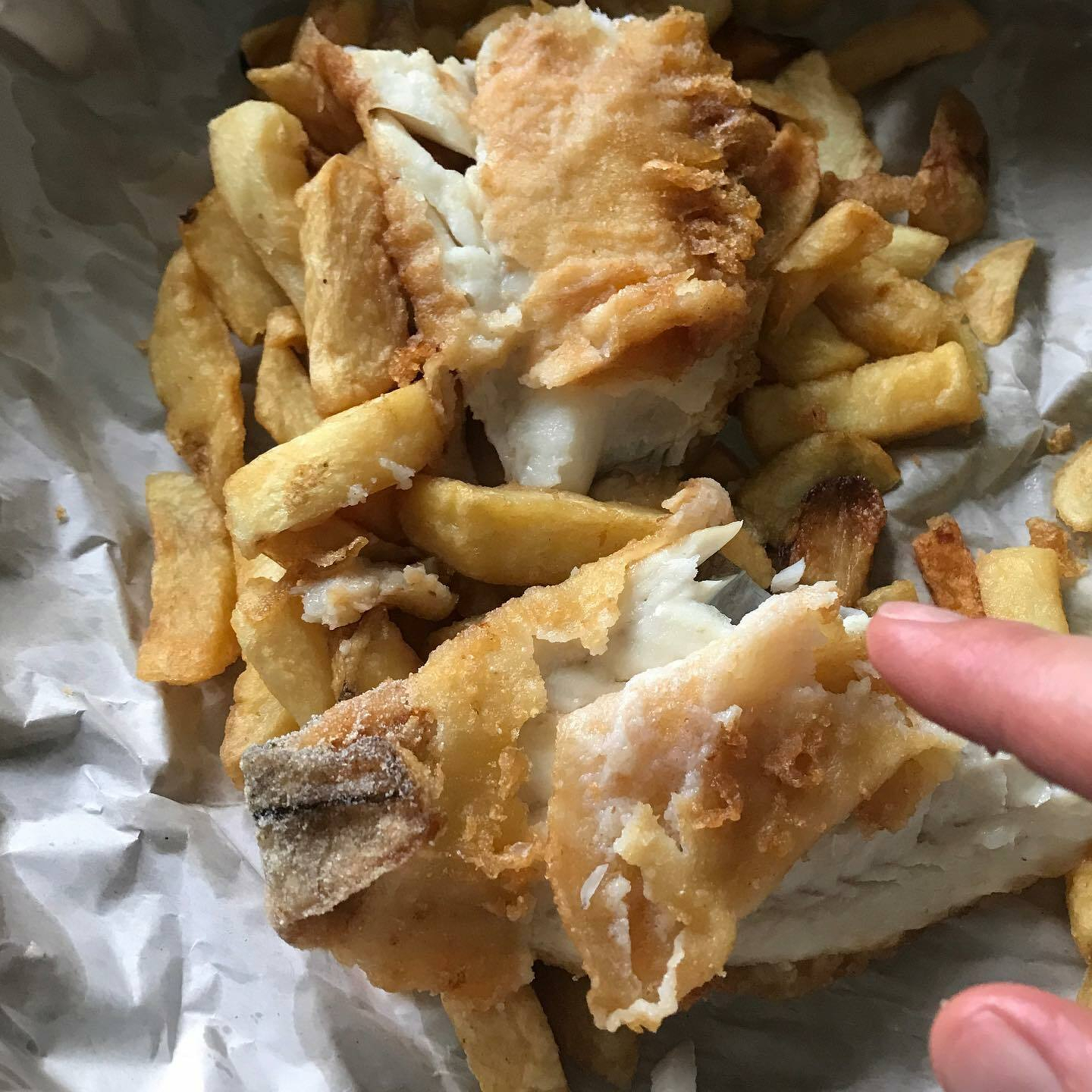 Deep-fried fish and chips are shown in a paper container.