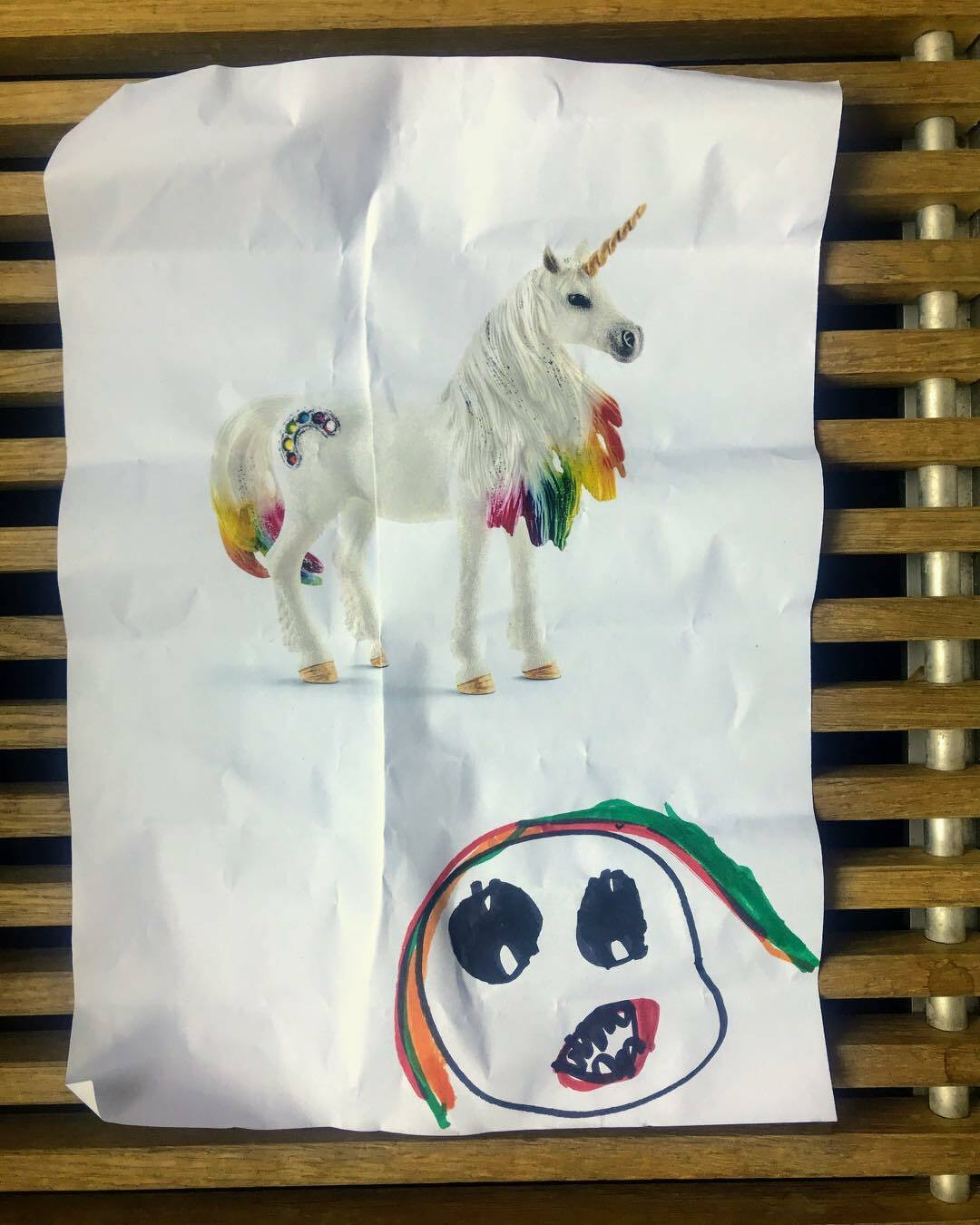 A white unicorn with a rainbow mane and tail stands next to a hand-drawn, cartoon-like skull.