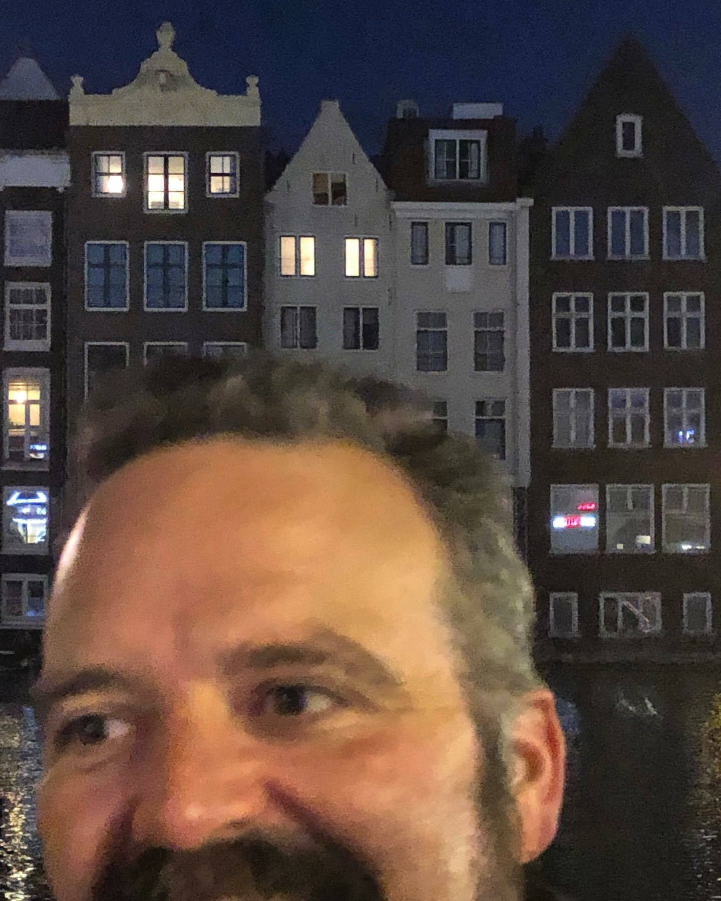A man’s face is partially visible with a blurred background of illuminated Dutch canal houses.
