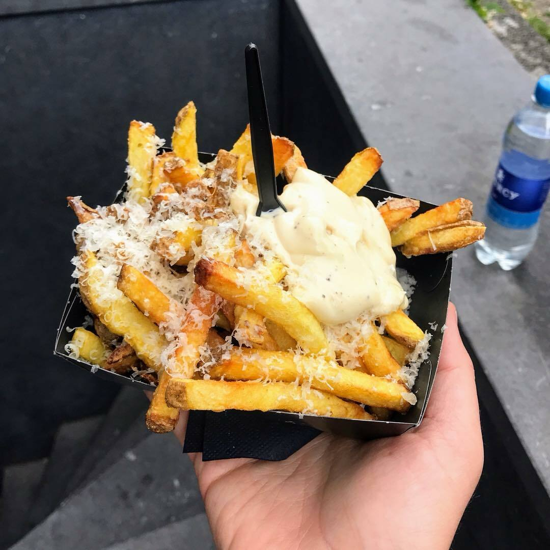 Hand holding a black box containing fries topped with cheese and a dipping sauce.