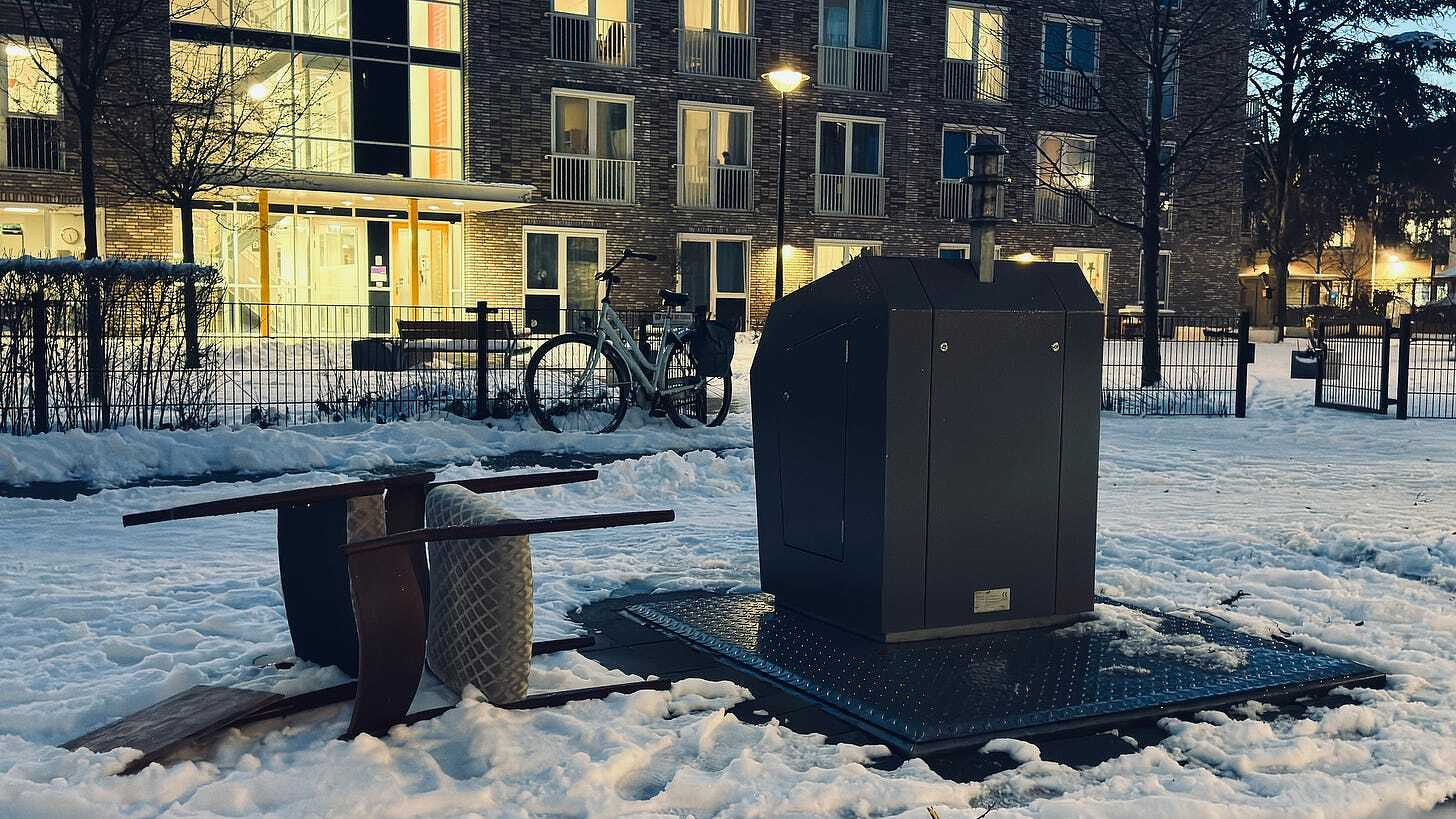 Auto-generated description: A snow-covered outdoor area features an overturned table, a chair, a bike, and a large metal container near an apartment building at dusk. Auto-generated description: A snow-covered outdoor area features an overturned table, a chair, a bike, and a large metal container near an apartment building at dusk.
