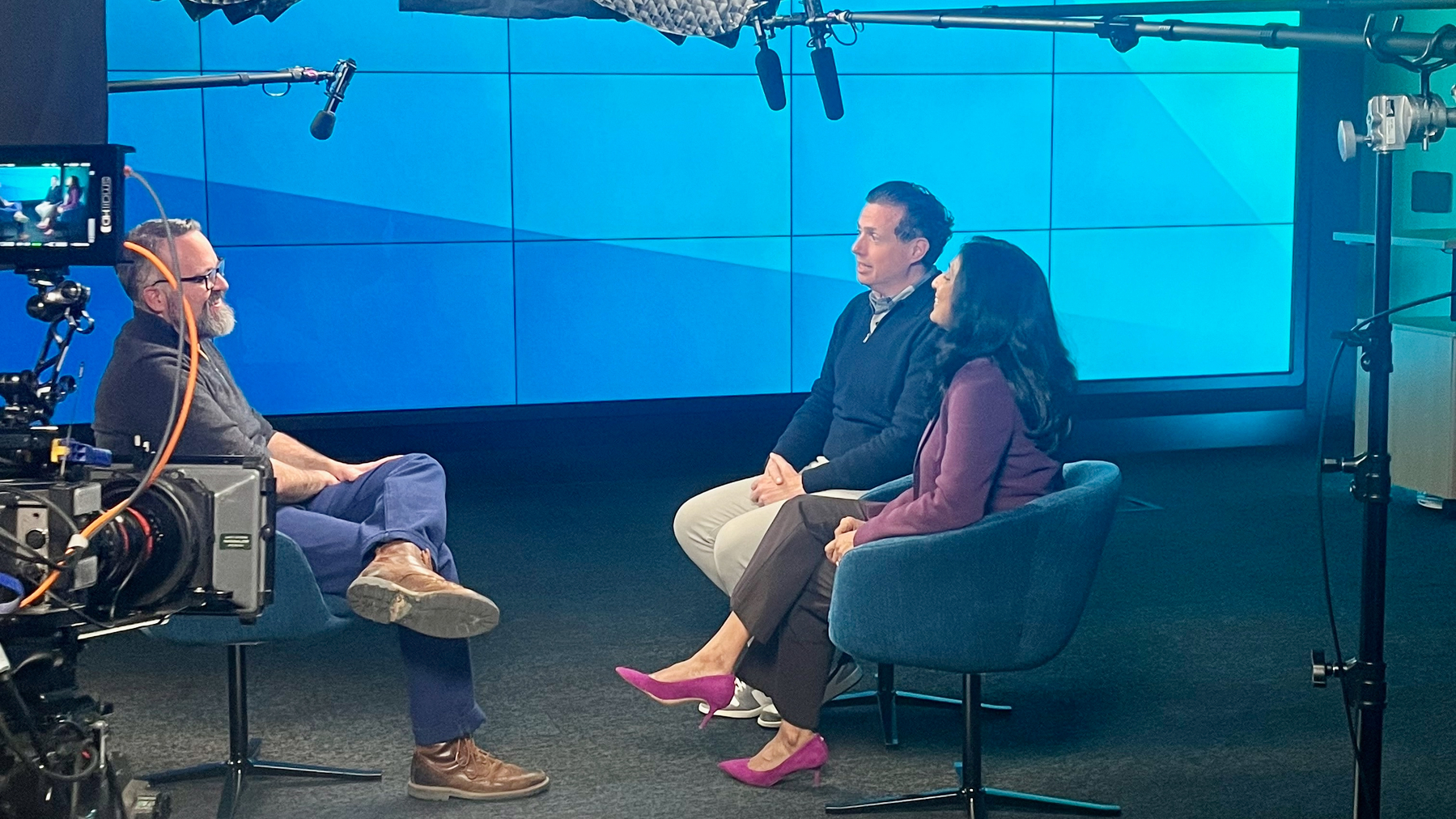 A man and woman sit in a studio with a camera and microphones, likely during a broadcast.