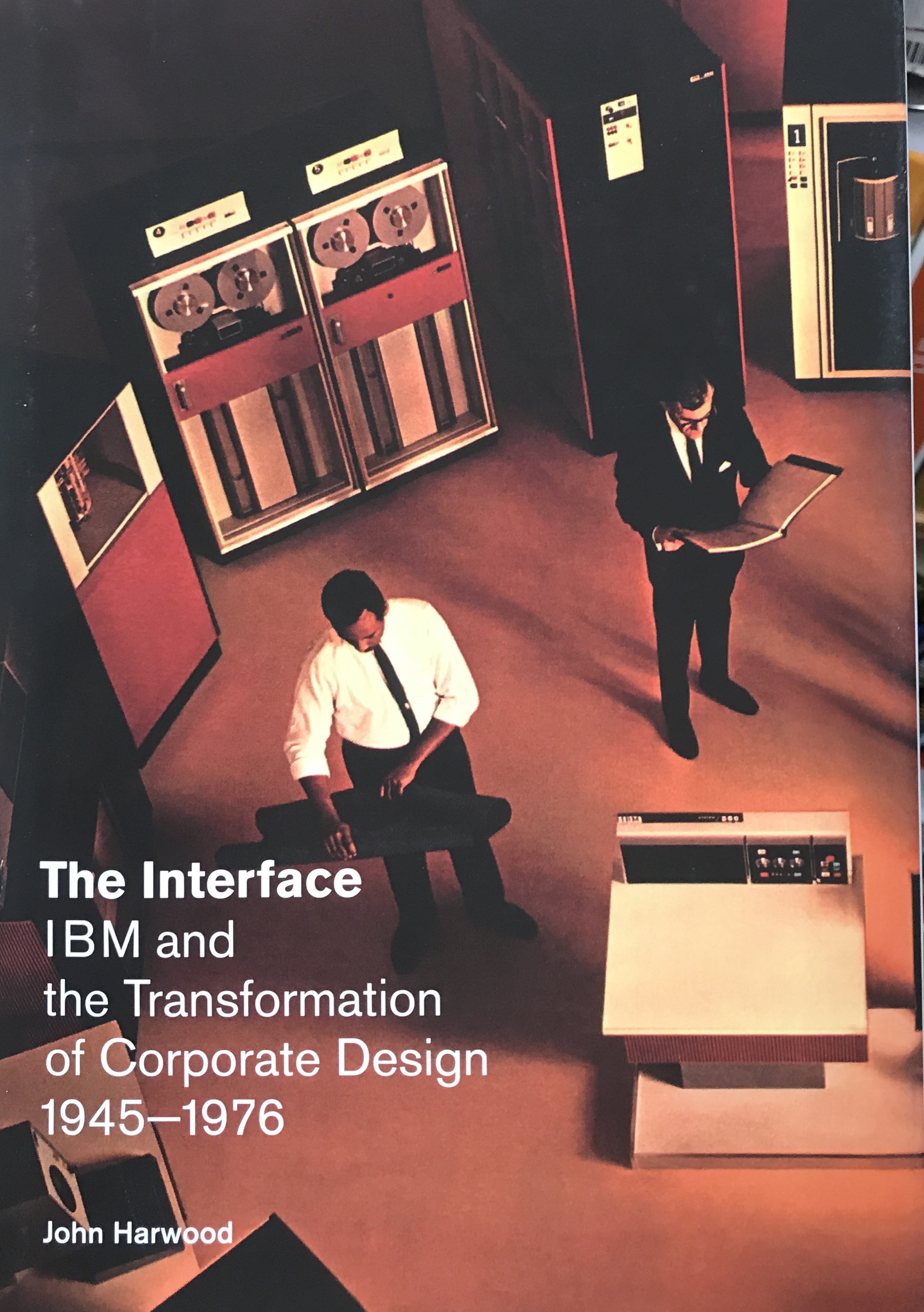 A man sits reviewing a diagram of IBM mainframe computers and corporate design transformation from 1945-1976.