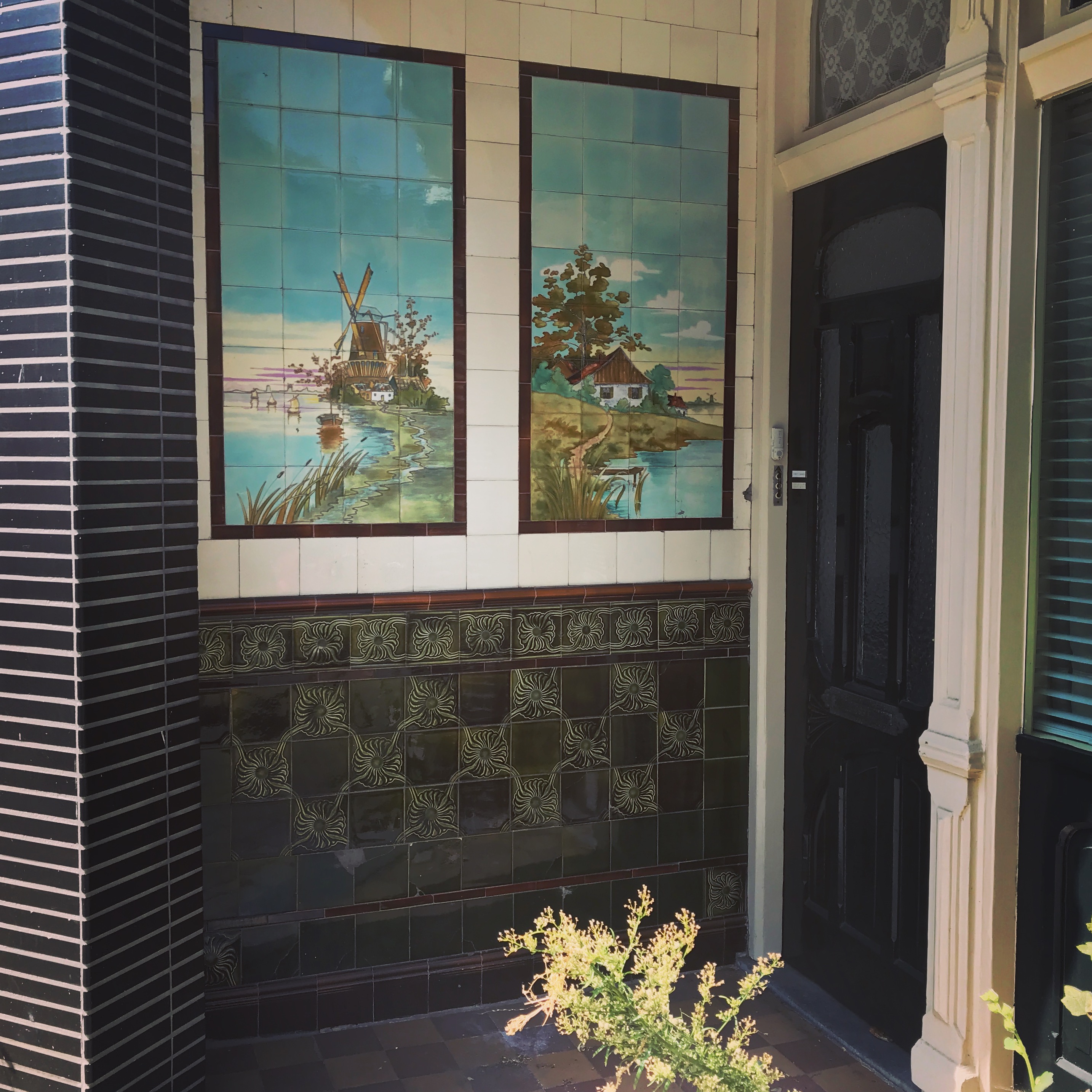 A dark-framed doorway is flanked by two decorative ceramic tiles depicting a windmill scene and a rural landscape.
