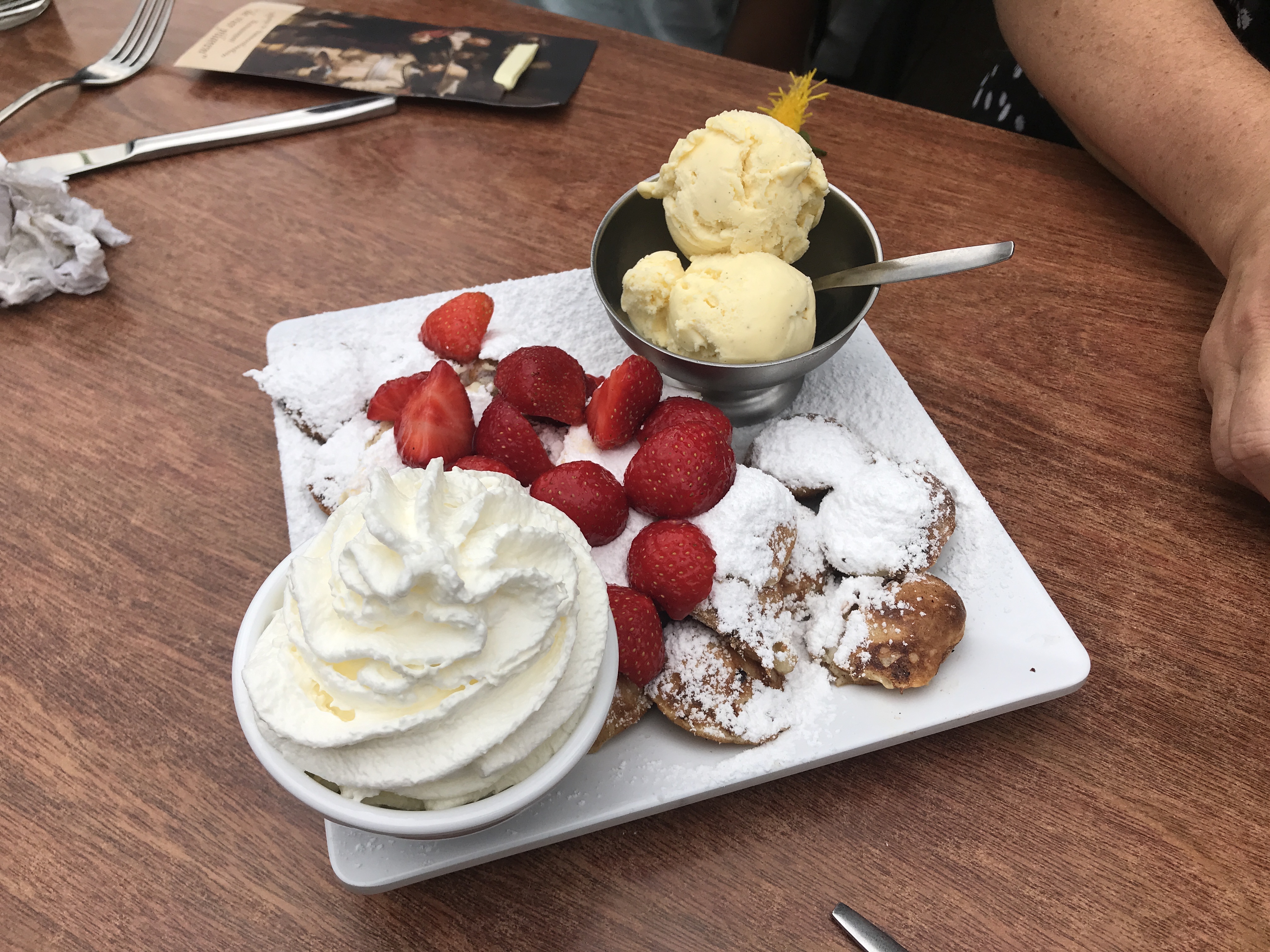 A white plate holds dusted Belgian waffles topped with whipped cream, strawberries, and a scoop of vanilla ice cream.