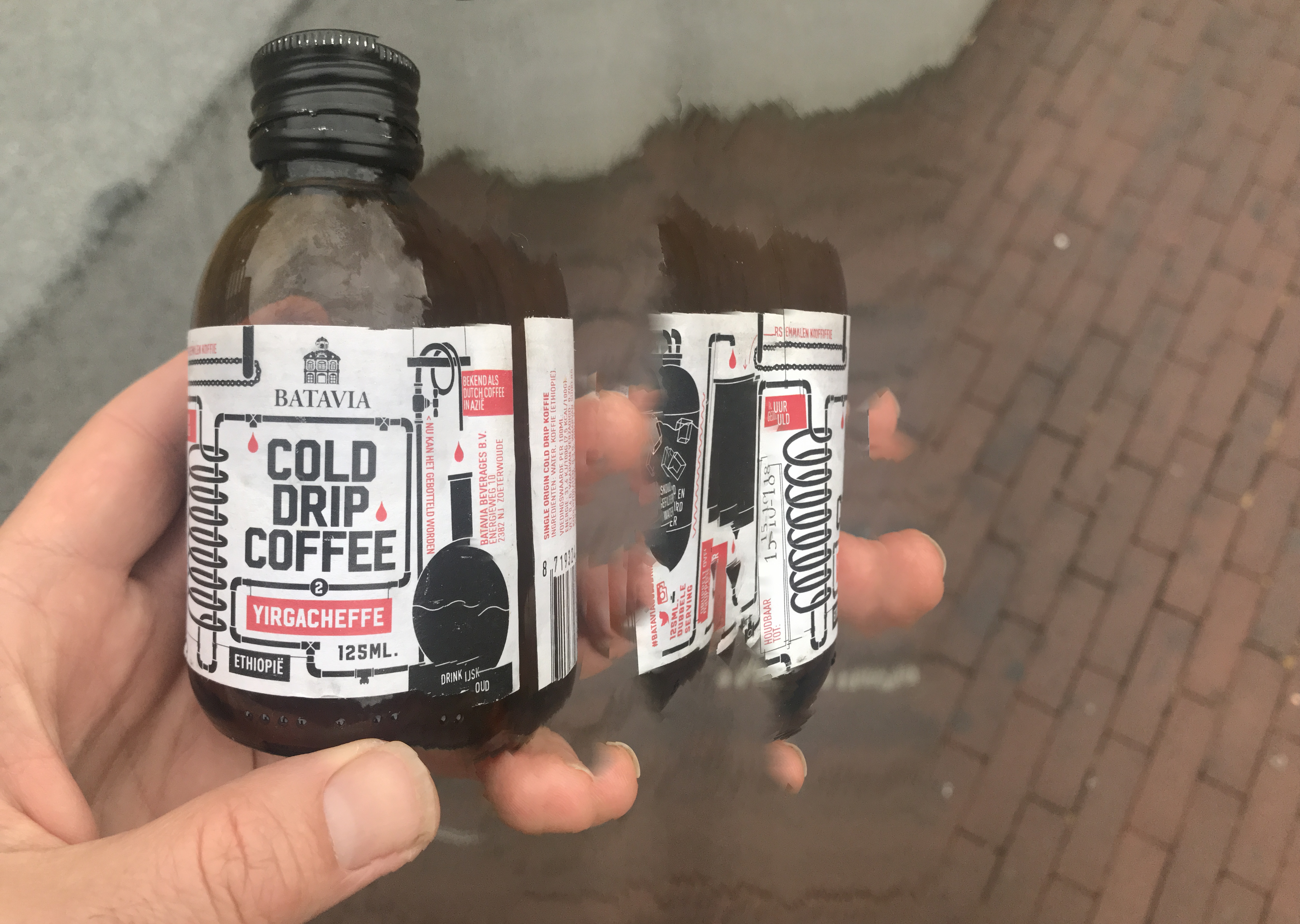 A hand holds a bottle of Batavia Cold Drip Coffee Yirgacheffe, displaying "Batavia" and "Cold Drip Coffee" text.