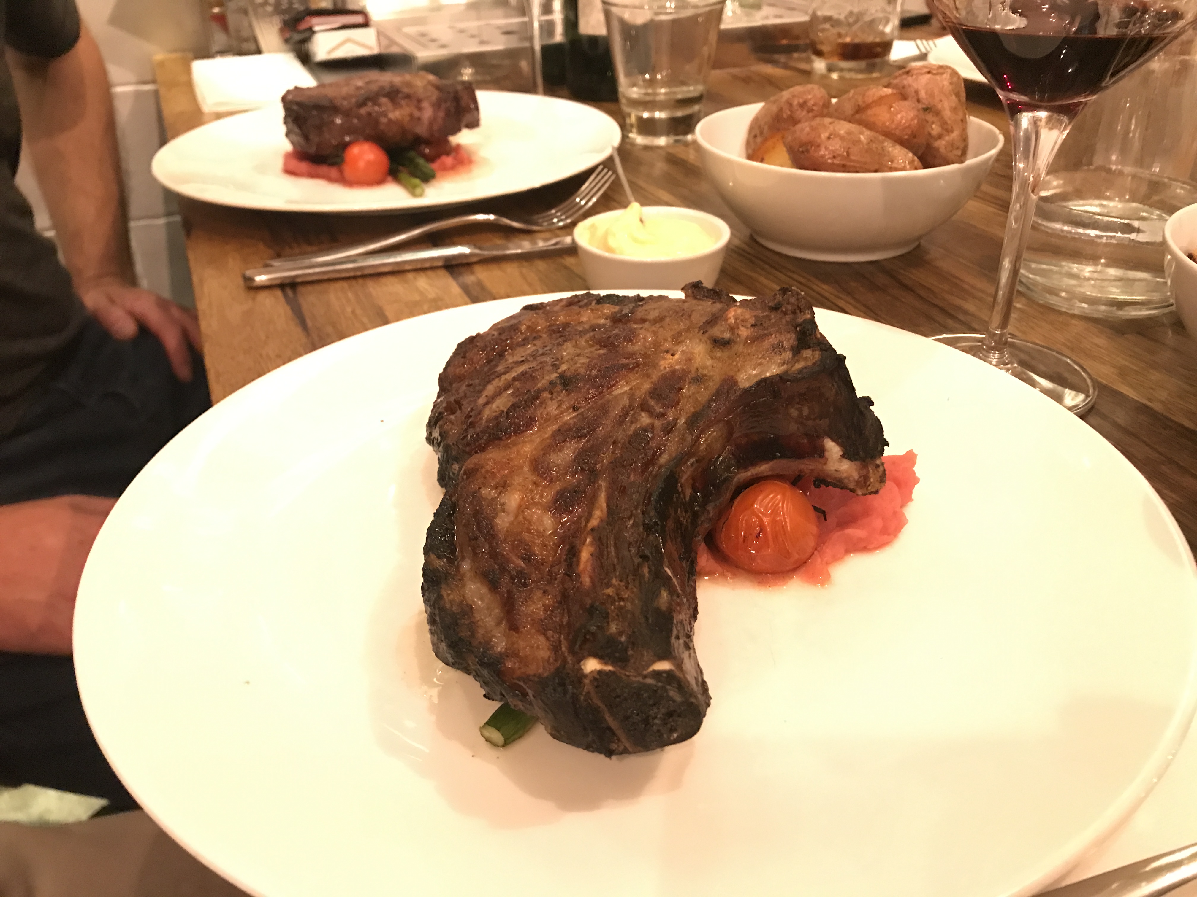 A large, cooked steak with a tomato garnish sits on a white plate.