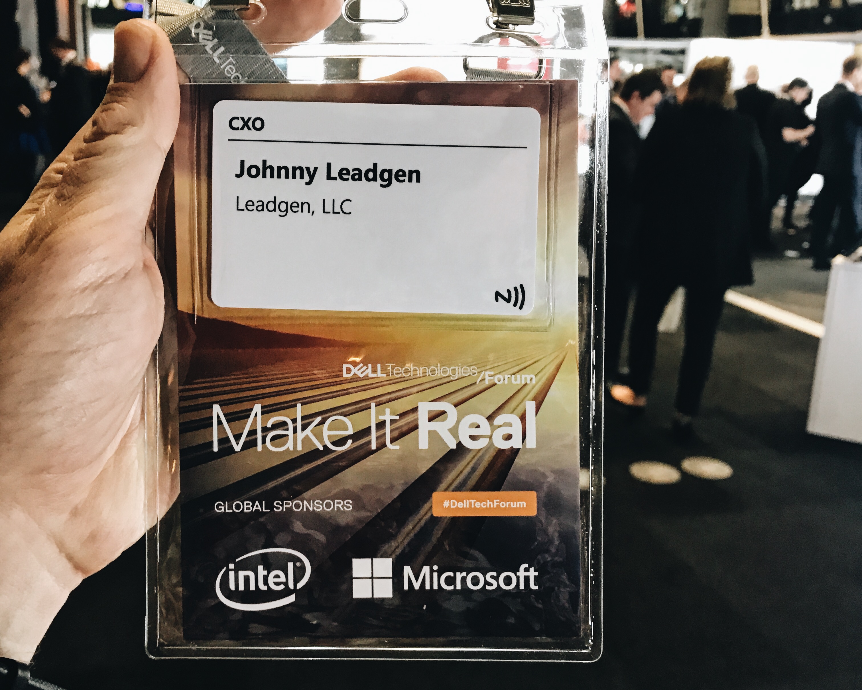 A hand holds a conference badge for Johnny Leadgen, LLC, featuring Dell Technologies and Microsoft logos.
