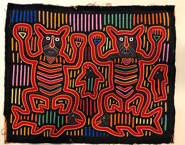 A black textile with red and multicolored embroidered figures and lines.