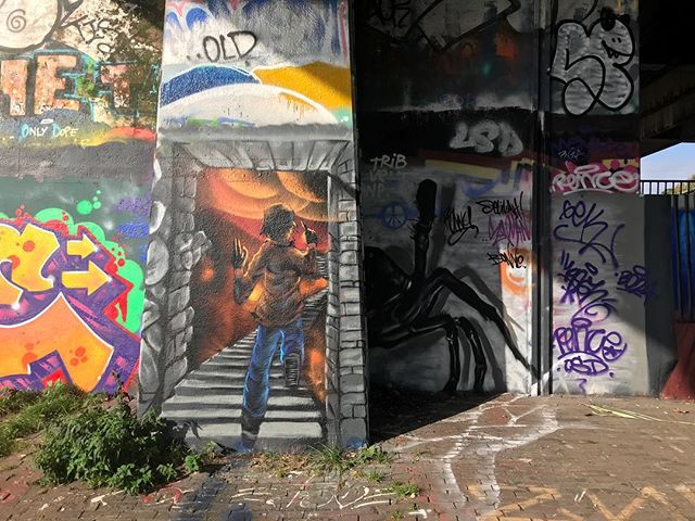 A colorful mural depicts a figure running down a staircase, with graffiti text visible on the surrounding concrete.