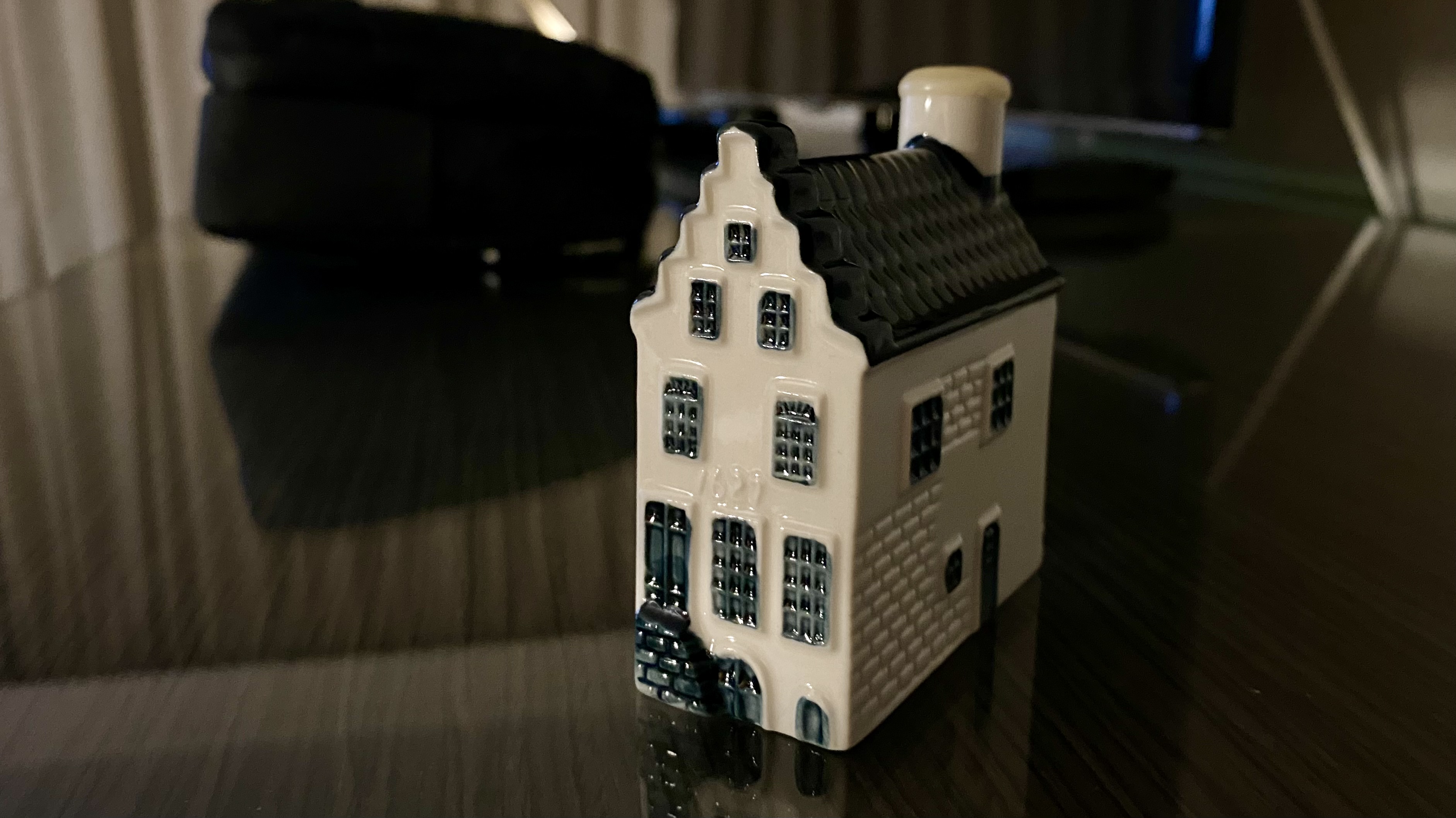 A small, white, Dutch-style house with multiple windows sits on a dark surface.