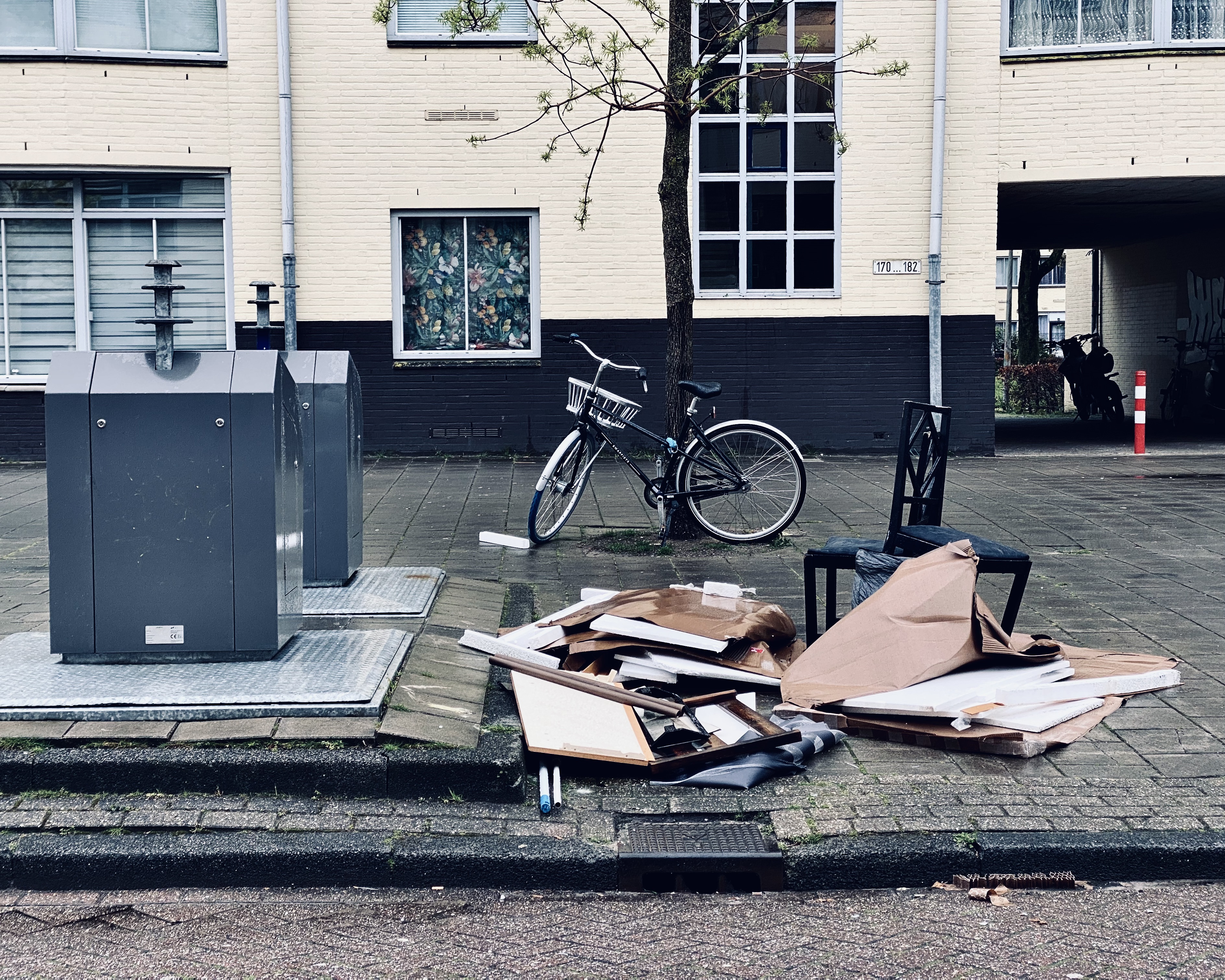 Discarded cardboard and a bicycle sit on a paved area in front of a building