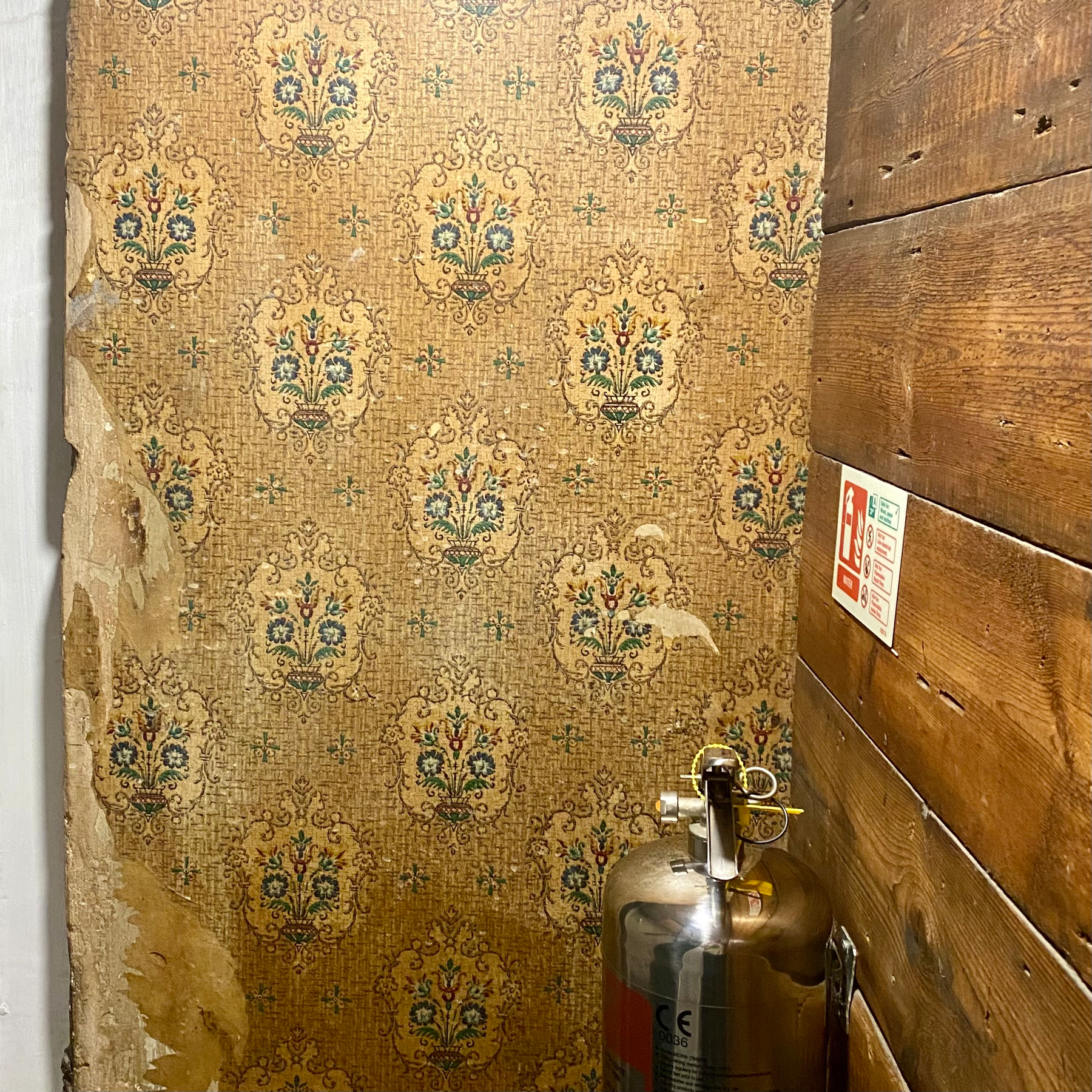 Wallpapered wall with a fire extinguisher and weathered wooden paneling