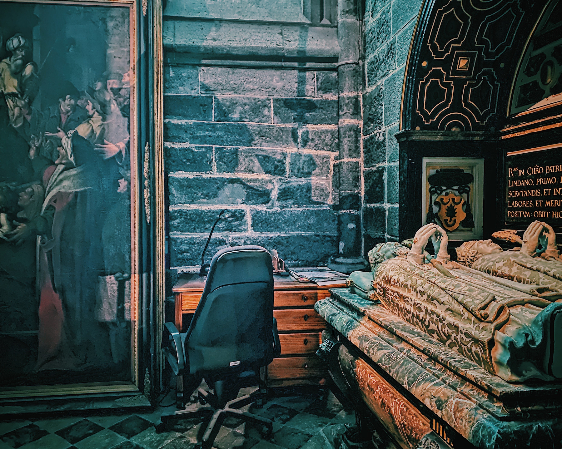 Ornate stone tomb, framed painting, and office chair in a dimly lit, historic interior