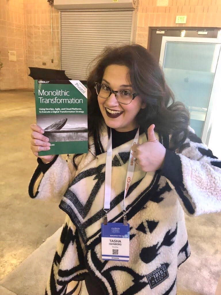Woman in a white shawl holds a book about monolithic transformation at a conference