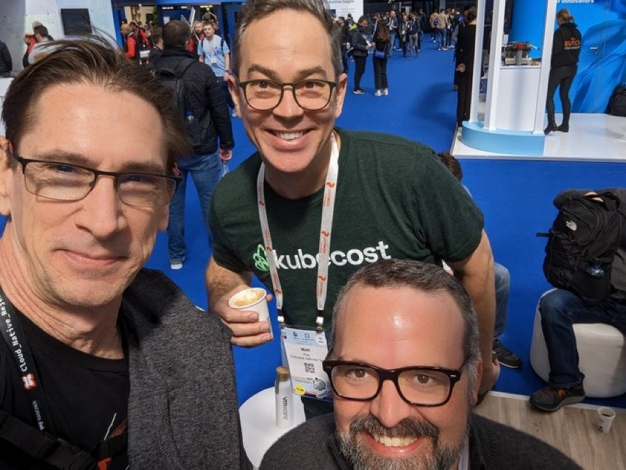 Three smiling men in glasses pose for a selfie at a tech conference