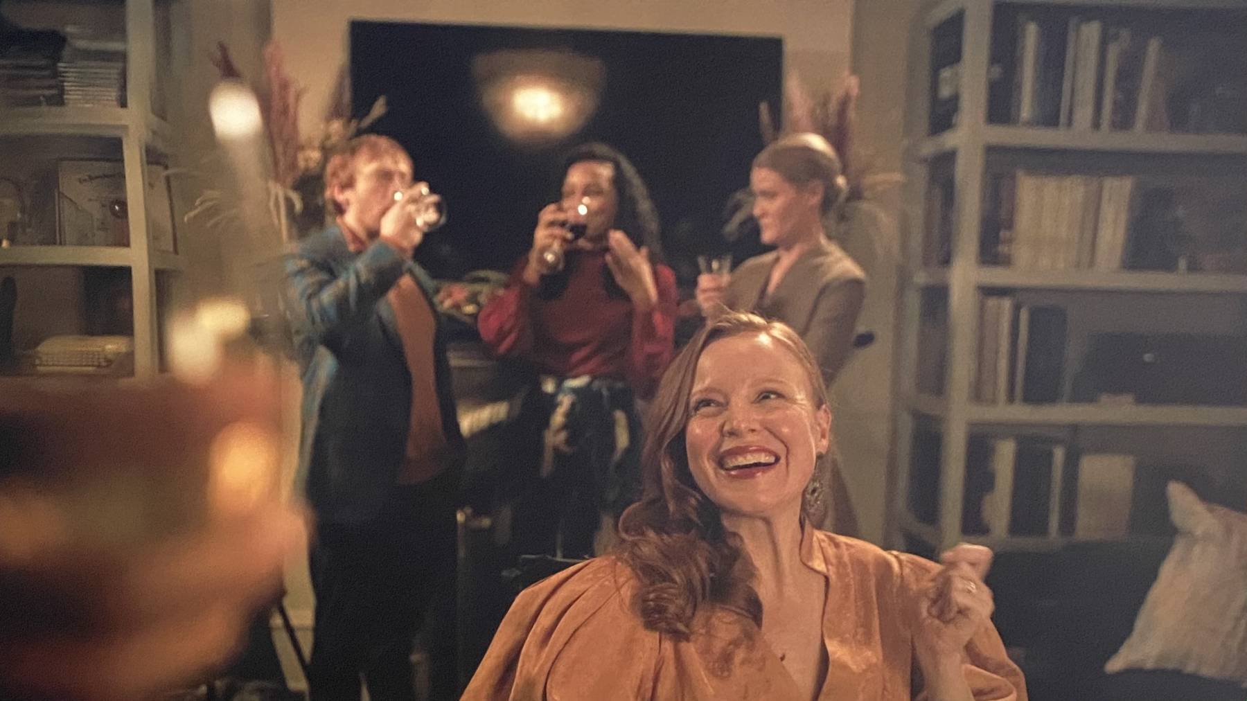 Smiling woman in orange dress, celebrating with friends in a warmly lit room
