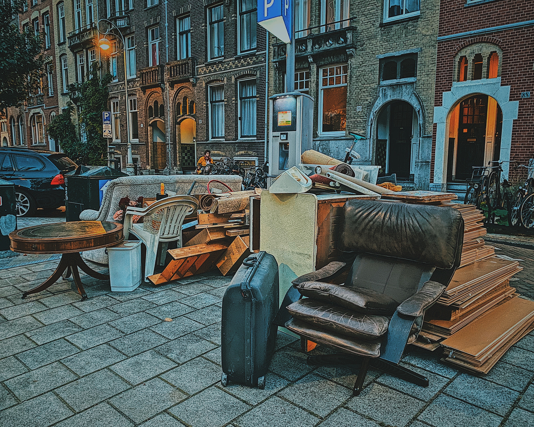 Discarded furniture and luggage piled on a street in front of buildings