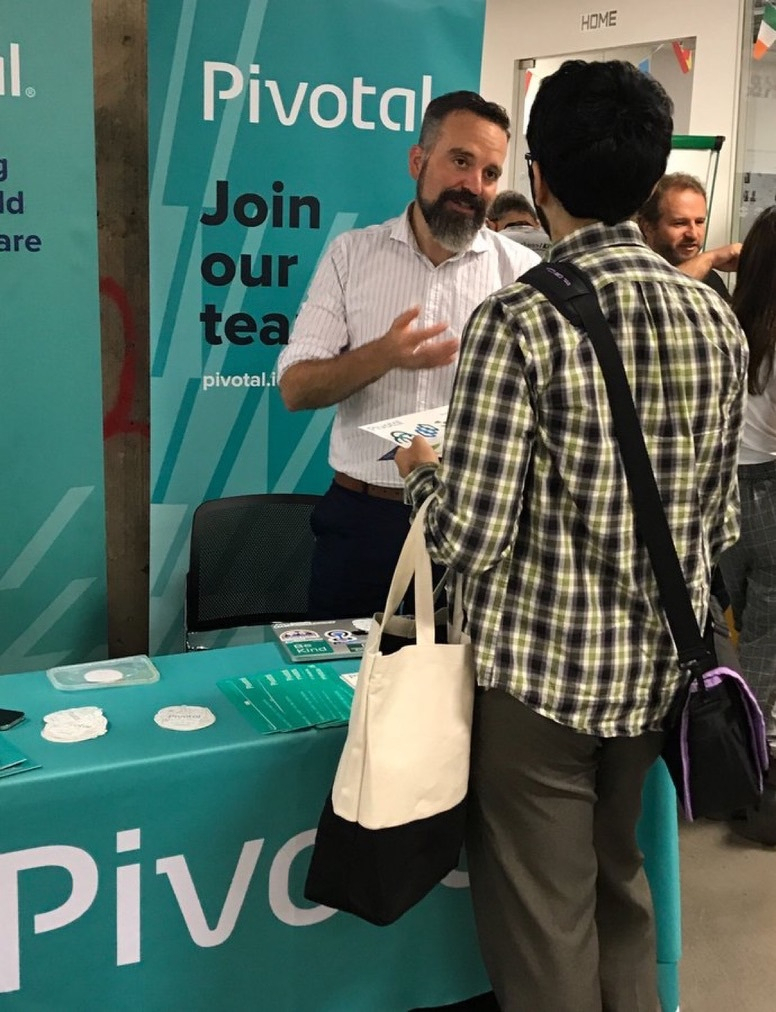 Man in a white shirt talks with another person at a table with a company banner