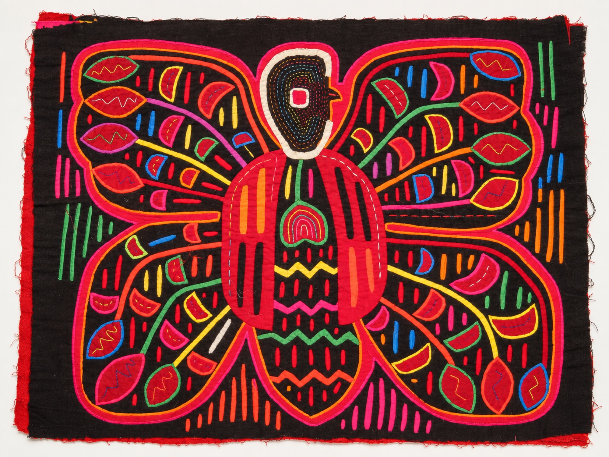 Symmetrical textile panel displaying a colorful butterfly with patterned wings and seed-like shapes against a dark fabric background.
