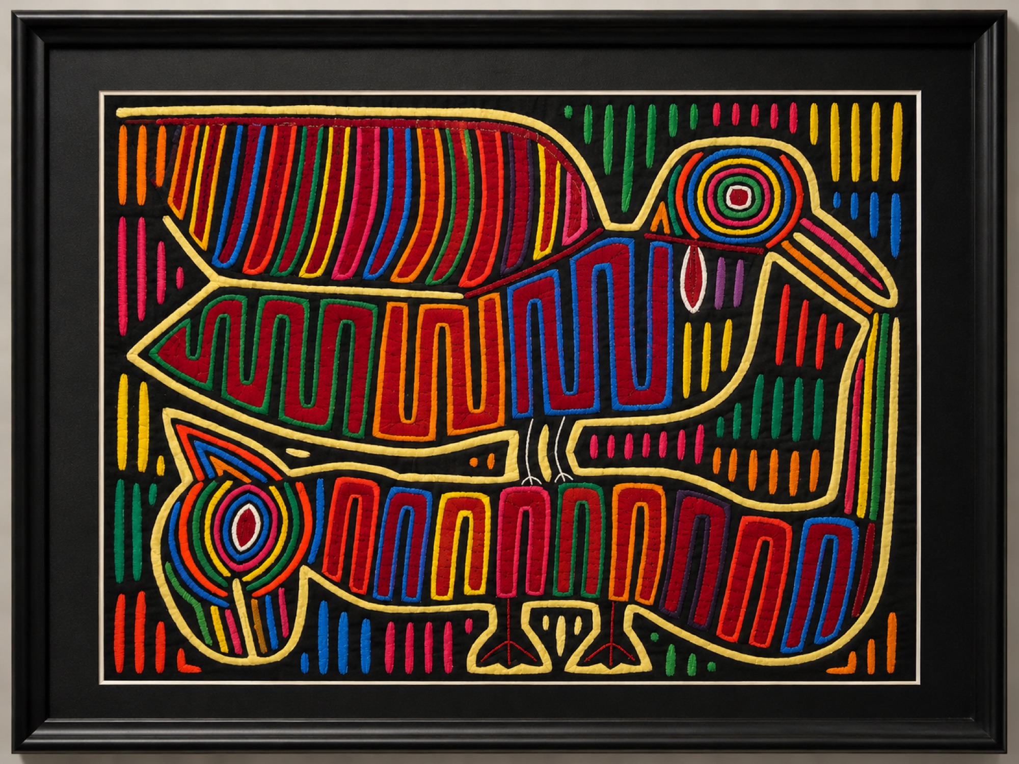 Framed textile artwork showing stylized colorful birds with concentric ring eyes against a dark background with stitched dashes.